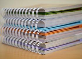 A colorful stack of spiral-bound notebooks neatly placed on a wooden desk. Ideal for educational themes.